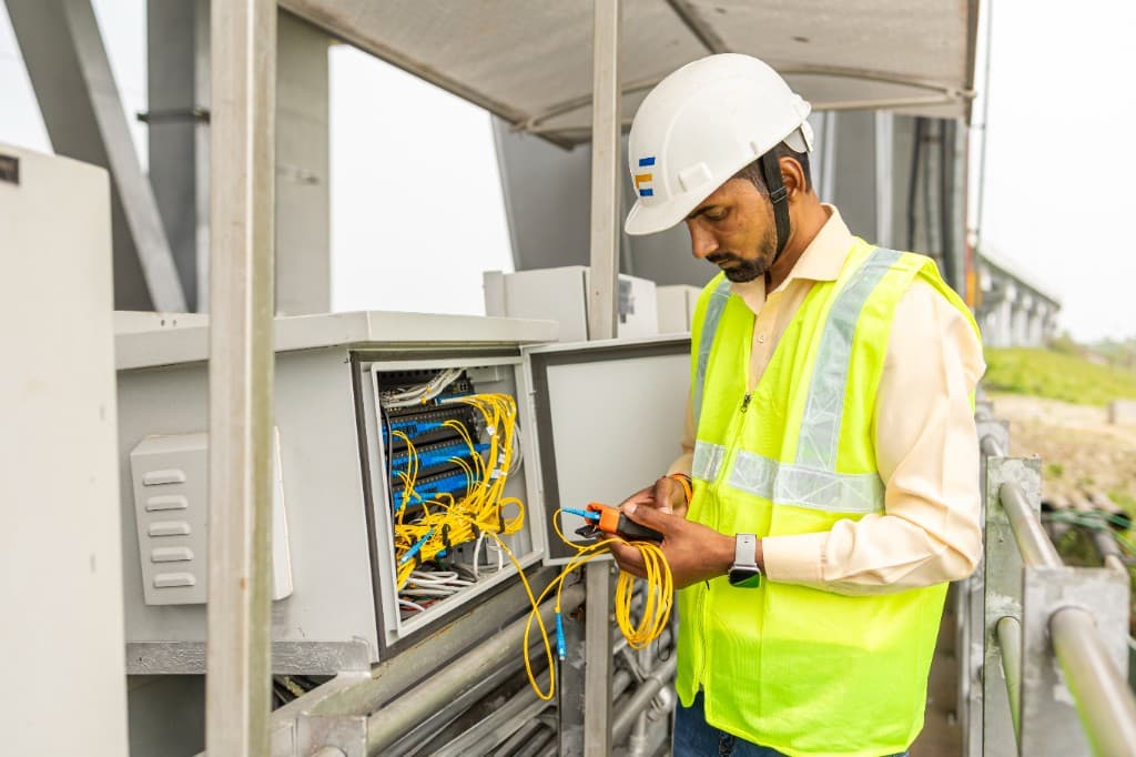 Technician in a hard hat working with fiber optic cables and field monitoring equipment